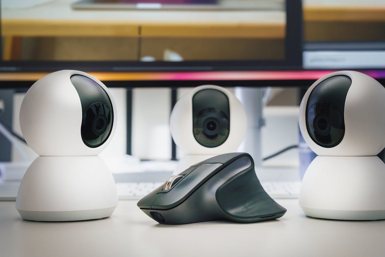 Three white webcams and a computer mouse on a desk, highlighting modern office technology.