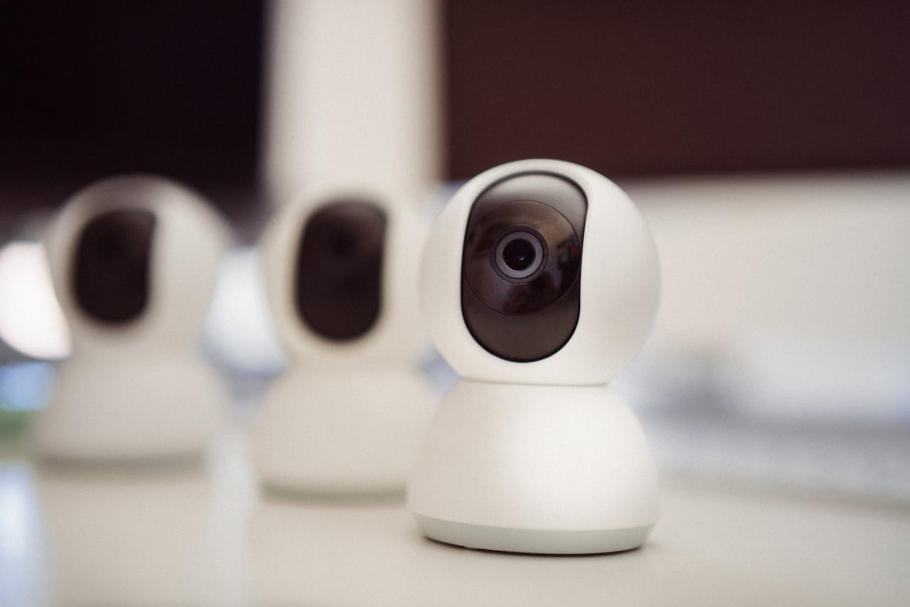 contact-img Close-up of three smart home security cameras placed on a white desk indoors.