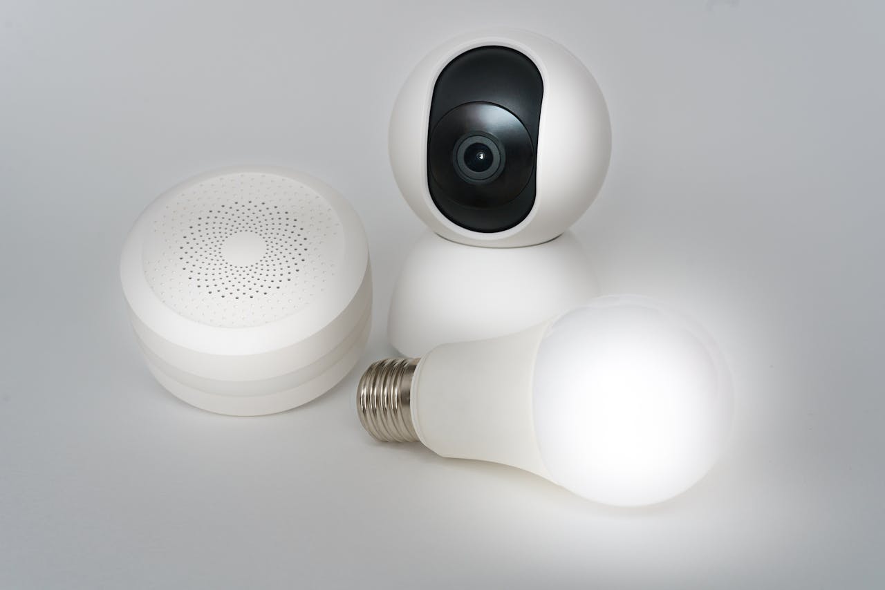 why-choose-us A set of smart home devices including a camera, speaker, and lightbulb on a white background.