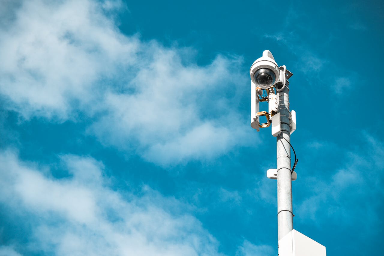 about-02 Close-up of a surveillance camera on a pole under a clear blue sky.