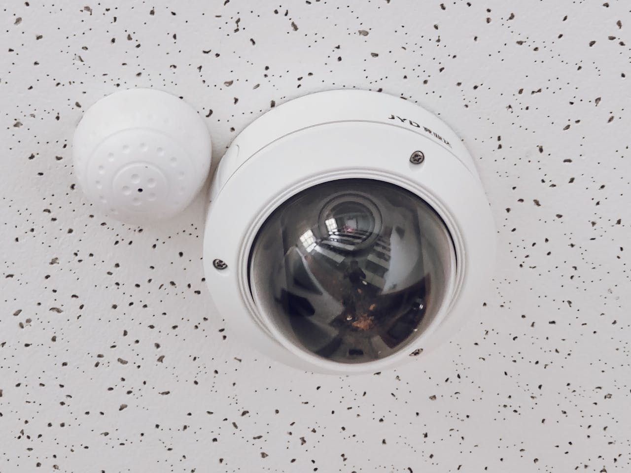 our-services-1 Close-up of a round dome surveillance camera installed on a speckled ceiling for security monitoring.